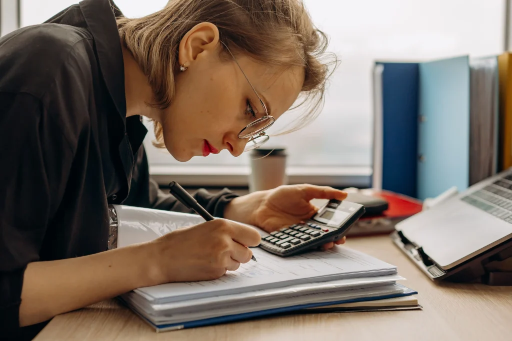 Gestionnaire de paie travaillant sur les fiches de paies avec une calculatrice et des documents