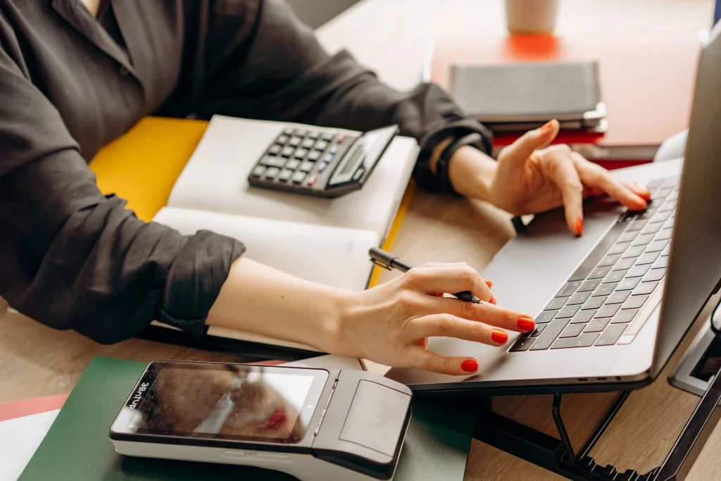 Gros plan sur une personne utilisant un ordinateur portable avec un terminal de paiement et une calculatrice sur le bureau