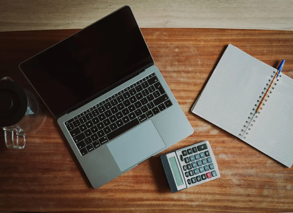 Vue de dessus d'un bureau avec un ordinateur portable, une calculatrice et un bloc-notes ouvert pour le travail